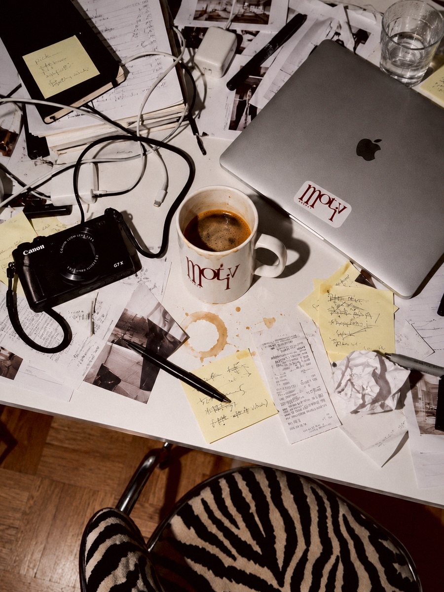 Arbeidsbord med kamera, notater og Motiv-kopp med kaffe